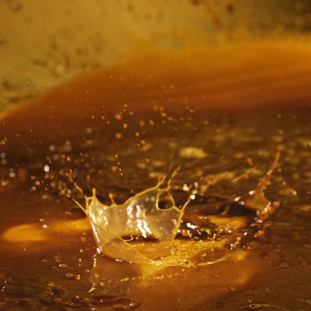 A drop of Sérum Vivant by Biologique Recherche falling into an amber liquid