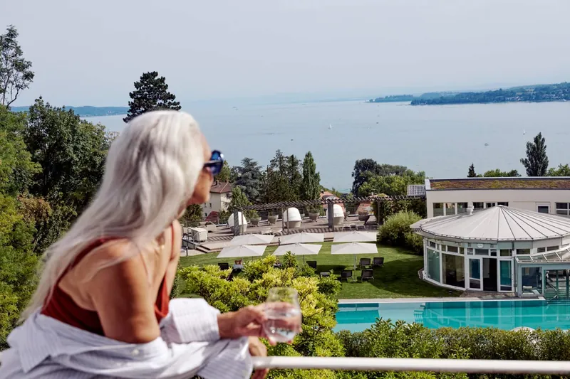 Woman with a glass of water on a Buchinger Wilhelmi terrace above the garden, pool and lake