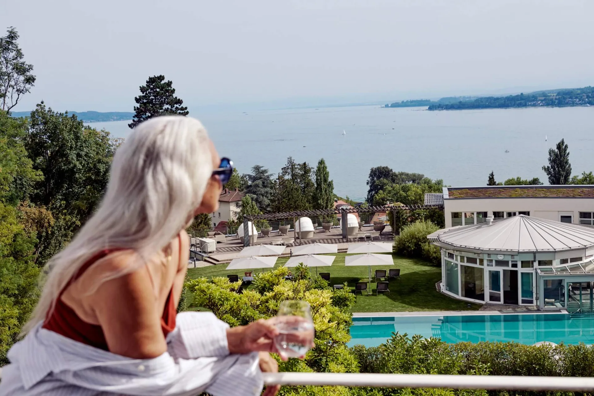 Woman with a glass of water on a Buchinger Wilhelmi terrace above the garden, pool and lake