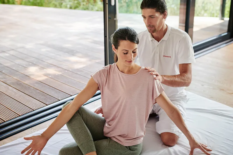 Yoga session at VIVAMAYR: a teacher adjusts the posture of a participant on the mat