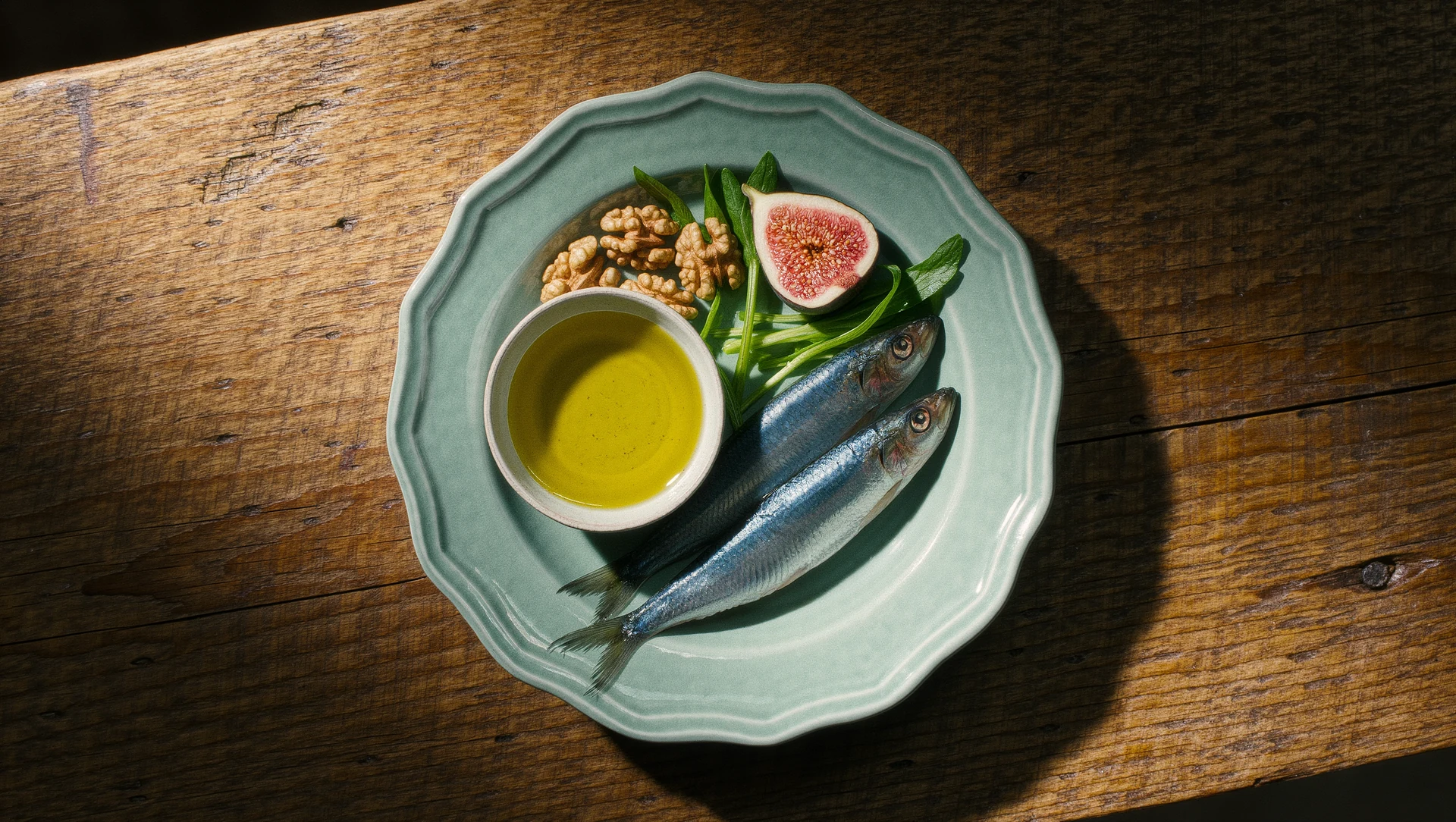 An overhead still life of a Mediterranean longevity plate: olive oil in a small ceramic bowl, walnuts